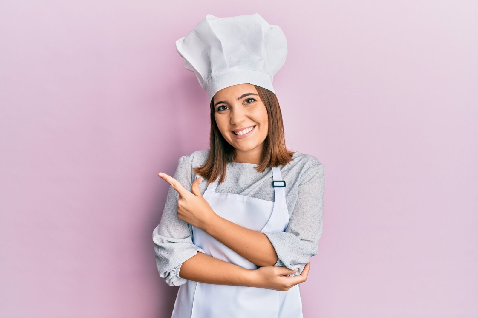Young beautiful woman wearing professional cook uniform and hat cheerful with a smile of face pointing with hand and finger up to the side with happy and natural expression on face Young beautiful woman wearing professional cook uniform and hat cheerful with a smile of face pointing with hand and finger up to the side with happy and natural expression on face